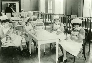 Four nurses, wearing face masks, feeding babies, c1940s