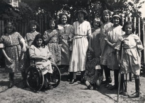 Group photo of a teacher and ten girls, one of whom is in a wheelchair and another is using a crutch; St Nicholas’ Orthopaedic Hospital and School, Pyrford, Surrey [1917]