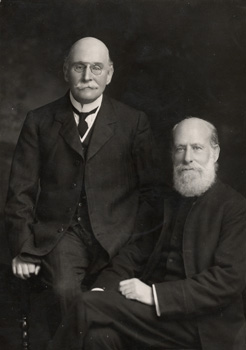 A portrait photograph of Robert and Edward Rudolf. Robert is standing and Edward is seated. Robert was 76 years old, and Edward was 80.
