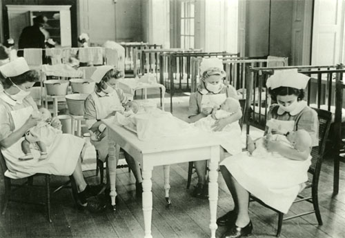 Four nurses, wearing face masks, feeding babies