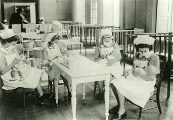 Four nurses, wearing face masks, feeding babies
